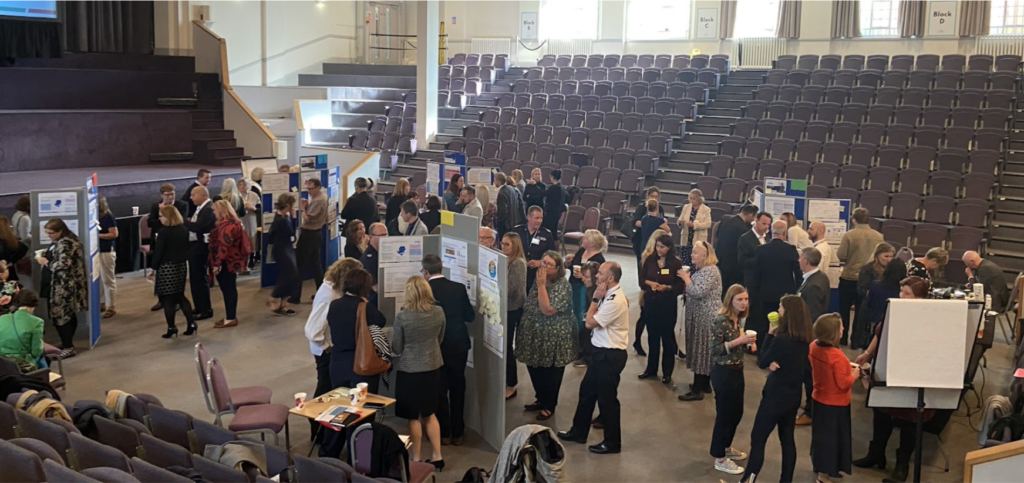 A busy hall with lots of delegates mingling, looking at posters